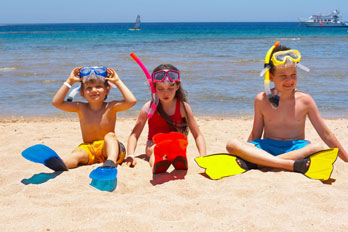 three children sitting on the sand at tyhe beach